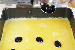 よく熱した卵焼き器に油を薄くひいて、かき混ぜた卵を流し入れます。上に黒豆をのせながら巻きつけていきます。